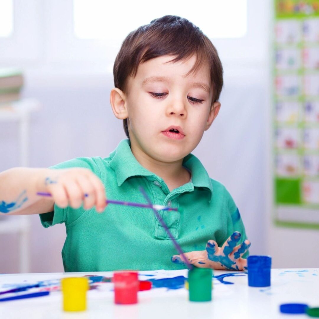 A young boy painting with a brush and colorful paints.
