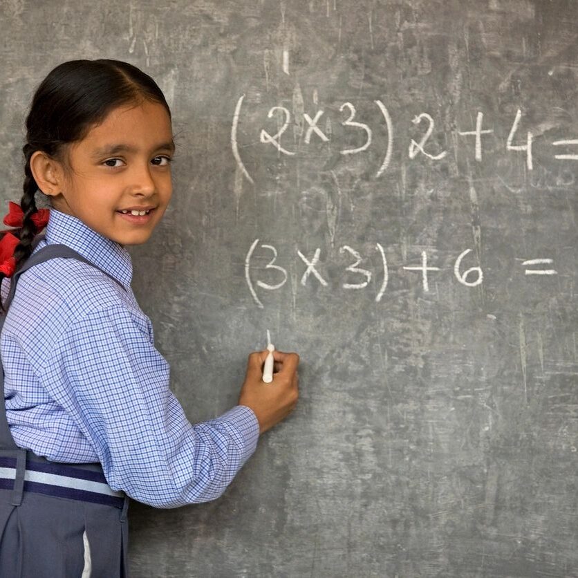 A girl solving math problems on a chalkboard.