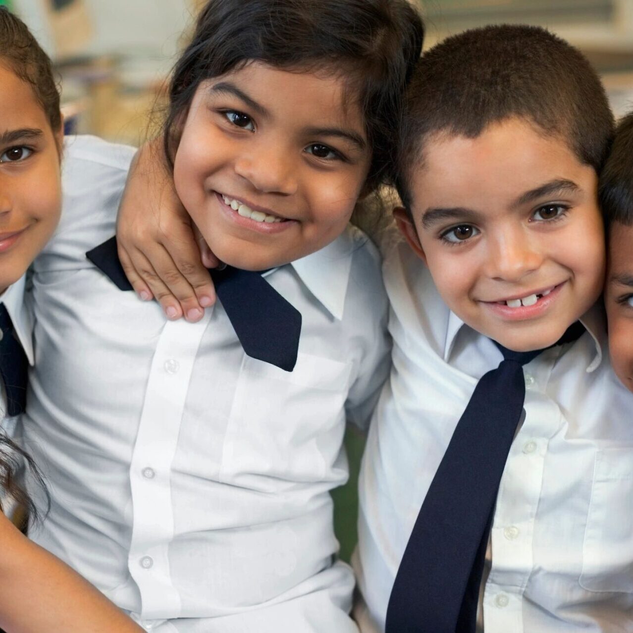 Three young children in white shirts and ties smiling together.